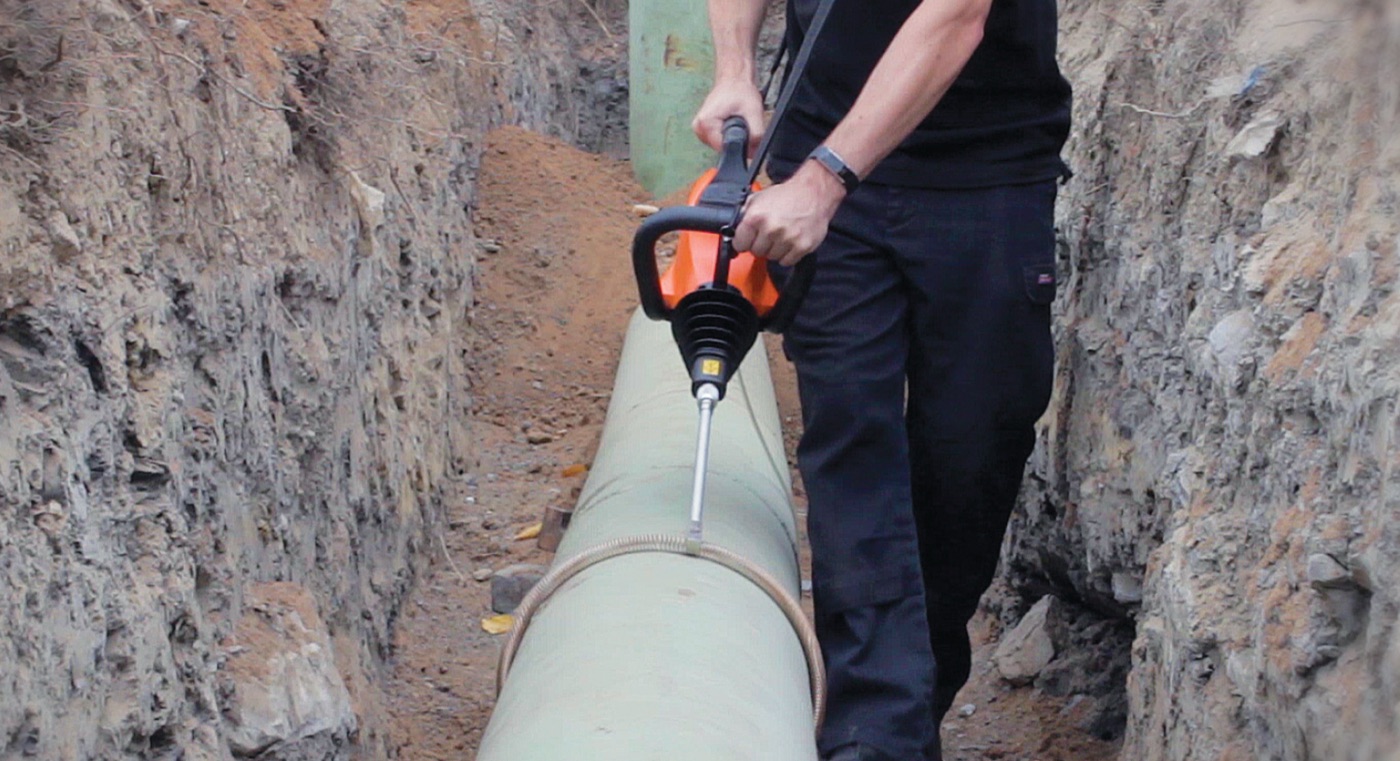 An inspector using an Elcometer holiday detector along a buried pipeline