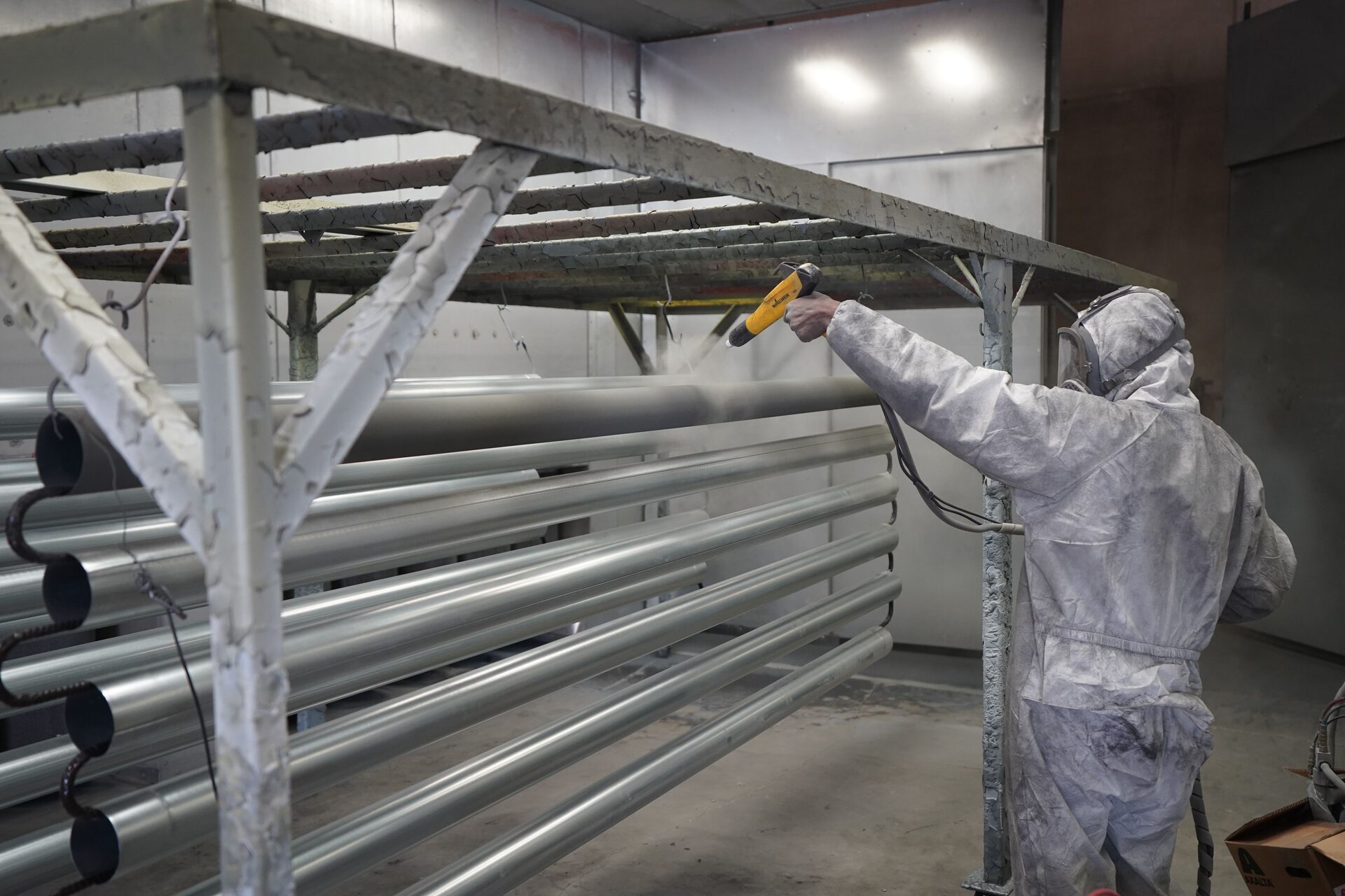Technician applying powder coating to steel pipes on a workshop coating line