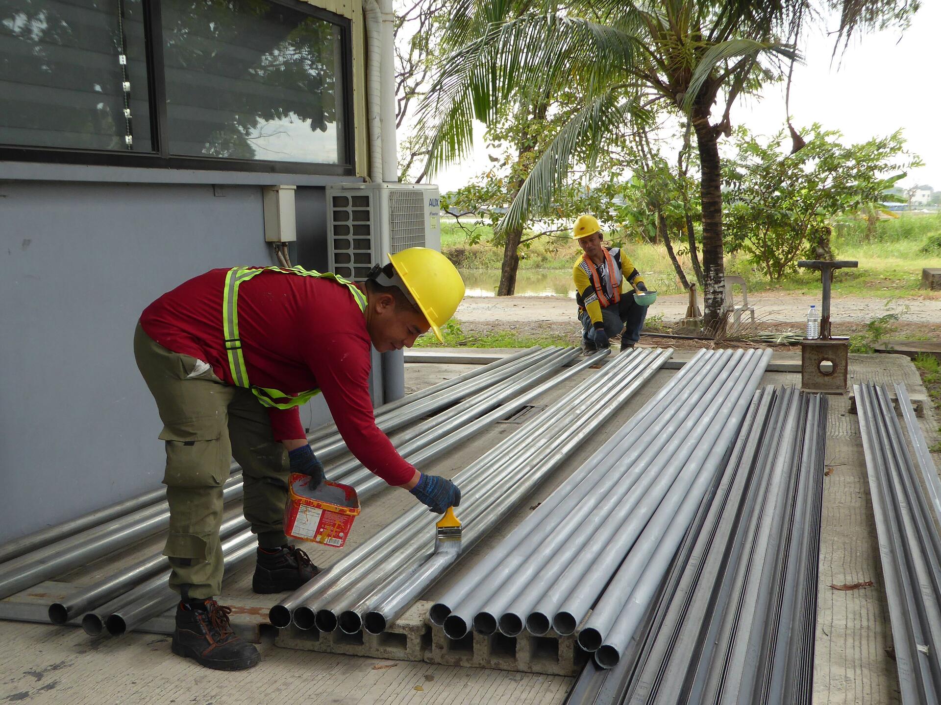 Site workers applying a protective coating to steel pipework outdoors