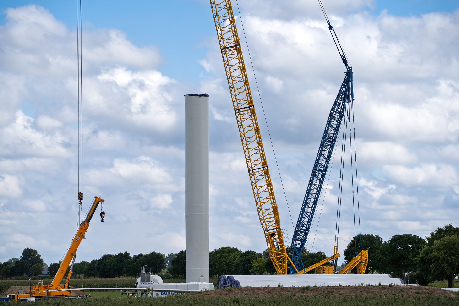 Cranes erecting a steel wind-turbine tower for coating and weld inspection